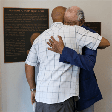 HAP Payne '68 hugs son in front of Plaque that bears his name