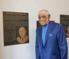 HAP Payne stands next to a plaque honoring him inside Payne Hall.