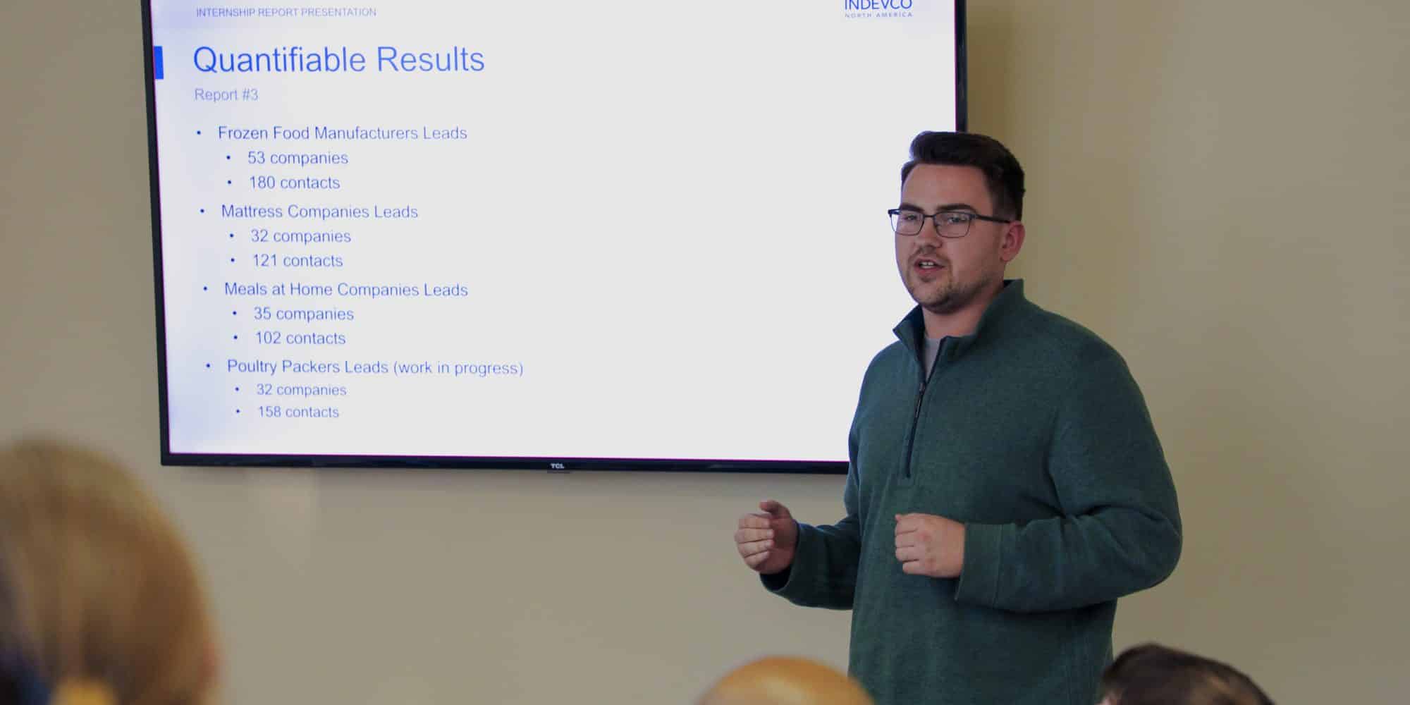 A Randolph-Macon student presenting business trends on a screen to an audience in a conference room.