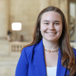 A young German woman in a blue blazer smiling.