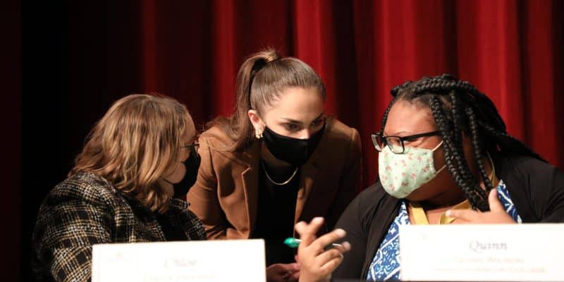Three students huddle over a table to discuss a question during the annual Ethics Bowl.