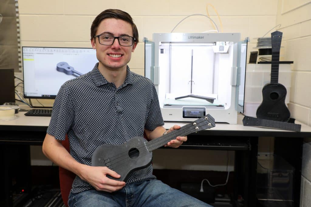 RMC Engineering student sitting next to a 3D printer