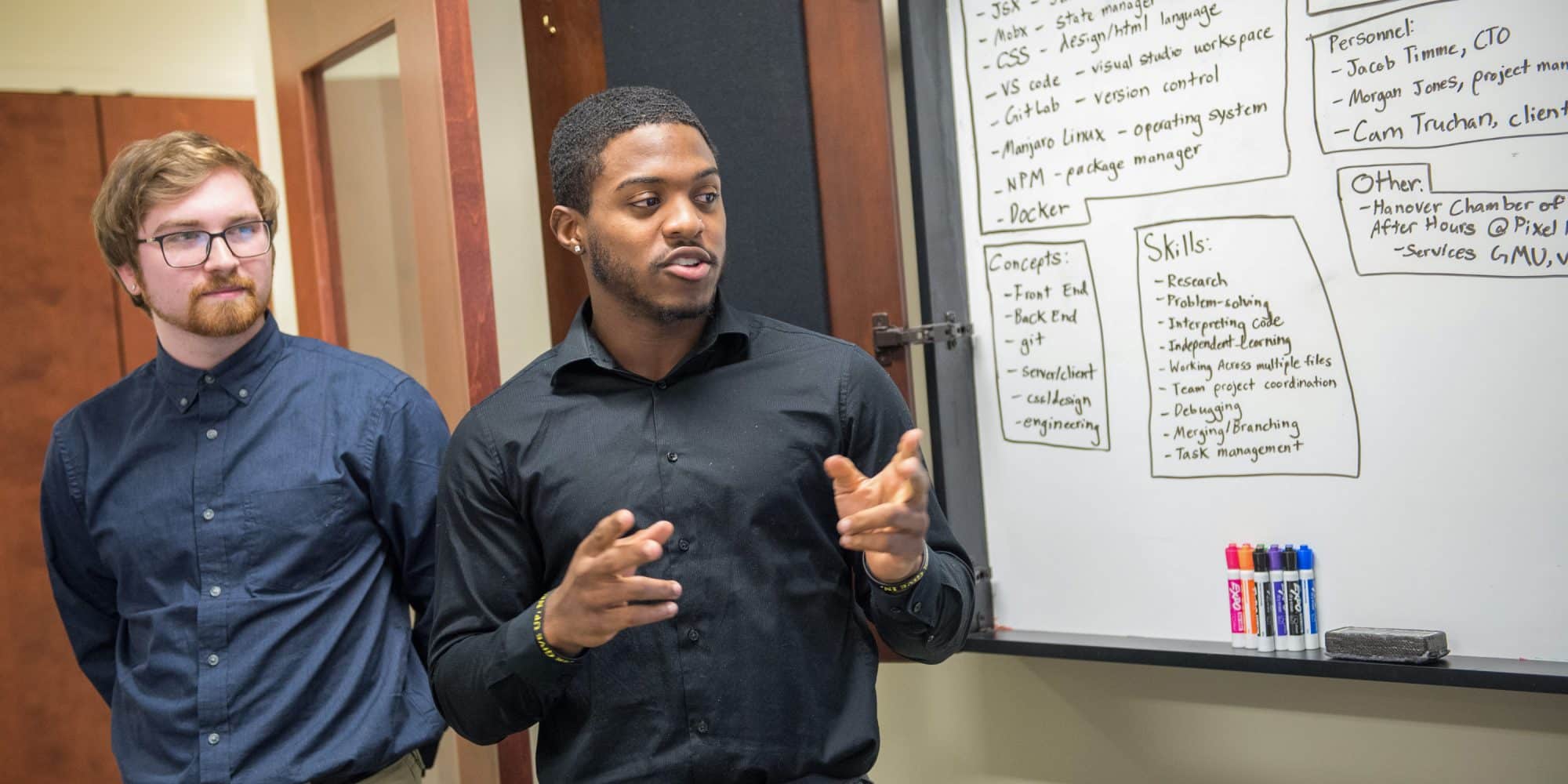 Students presenting in front of the class while referring to a white board
