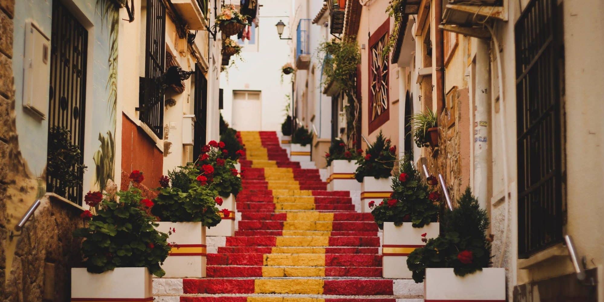 Narrow alley with a staircase painted in the colors of the spanish flag, lined with potted plants and traditional european buildings.