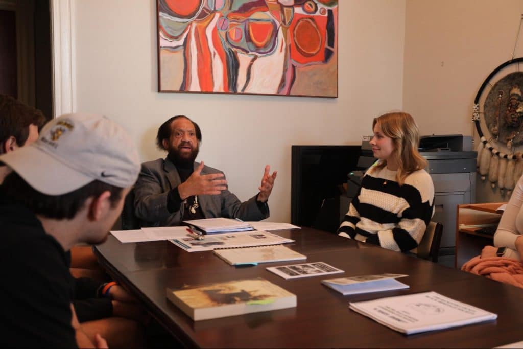 Black studies faculty member speaking with students while sitting at a table