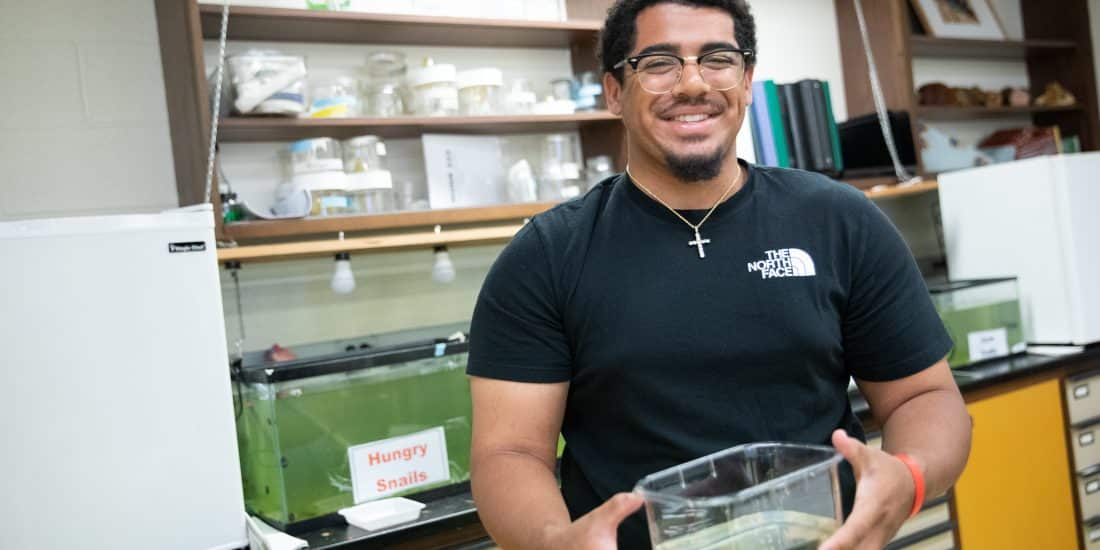 Studnet holding a bin with water in a lab
