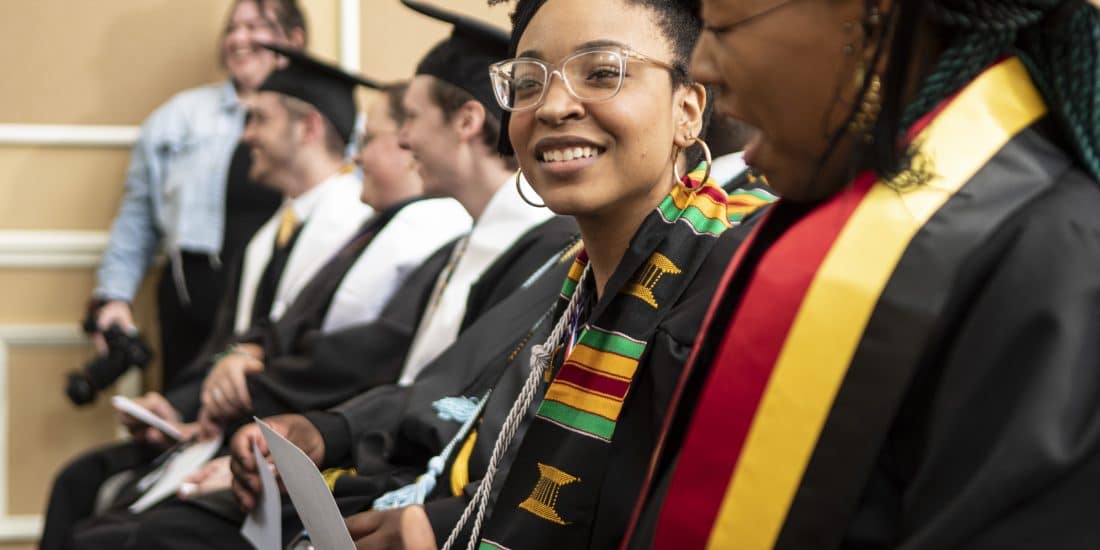 Female student in kente cloth and graduation regalia, looking forward