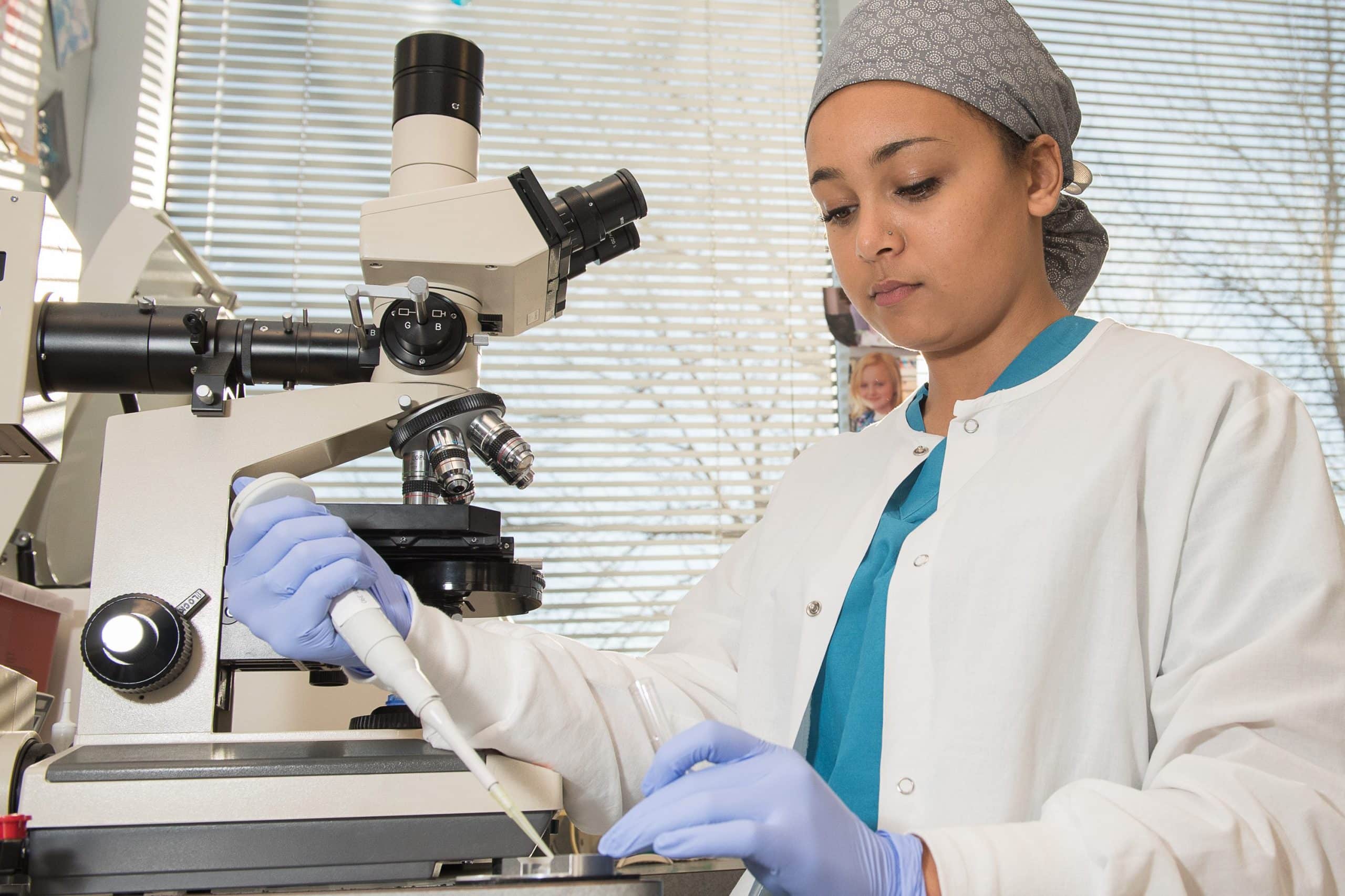 A RMC biology student poses in scrubs with lab equipment as part of an internship