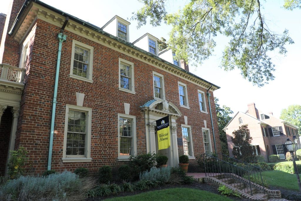 A photo of the Dalton House on campus with a yellow "Welcome Alumni" sign waving
