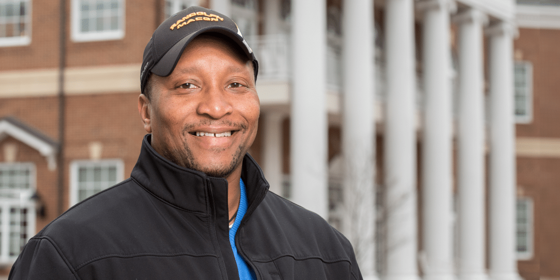 A black Dexter Hurt ’94 smiling in front of a building.