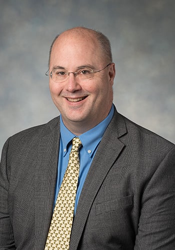 A bald man in a suit and tie receives prestigious awards from RMC in recognition of his outstanding work as a faculty member.