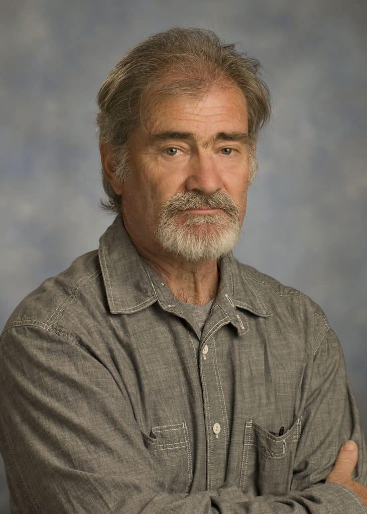 A faculty member with a beard and gray shirt is posing for a photo.
