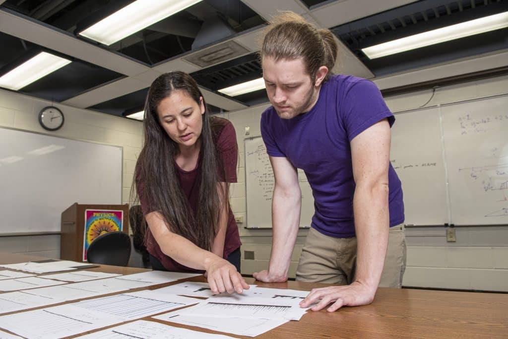 Professor with student studying physics equations in a classroom for research.
