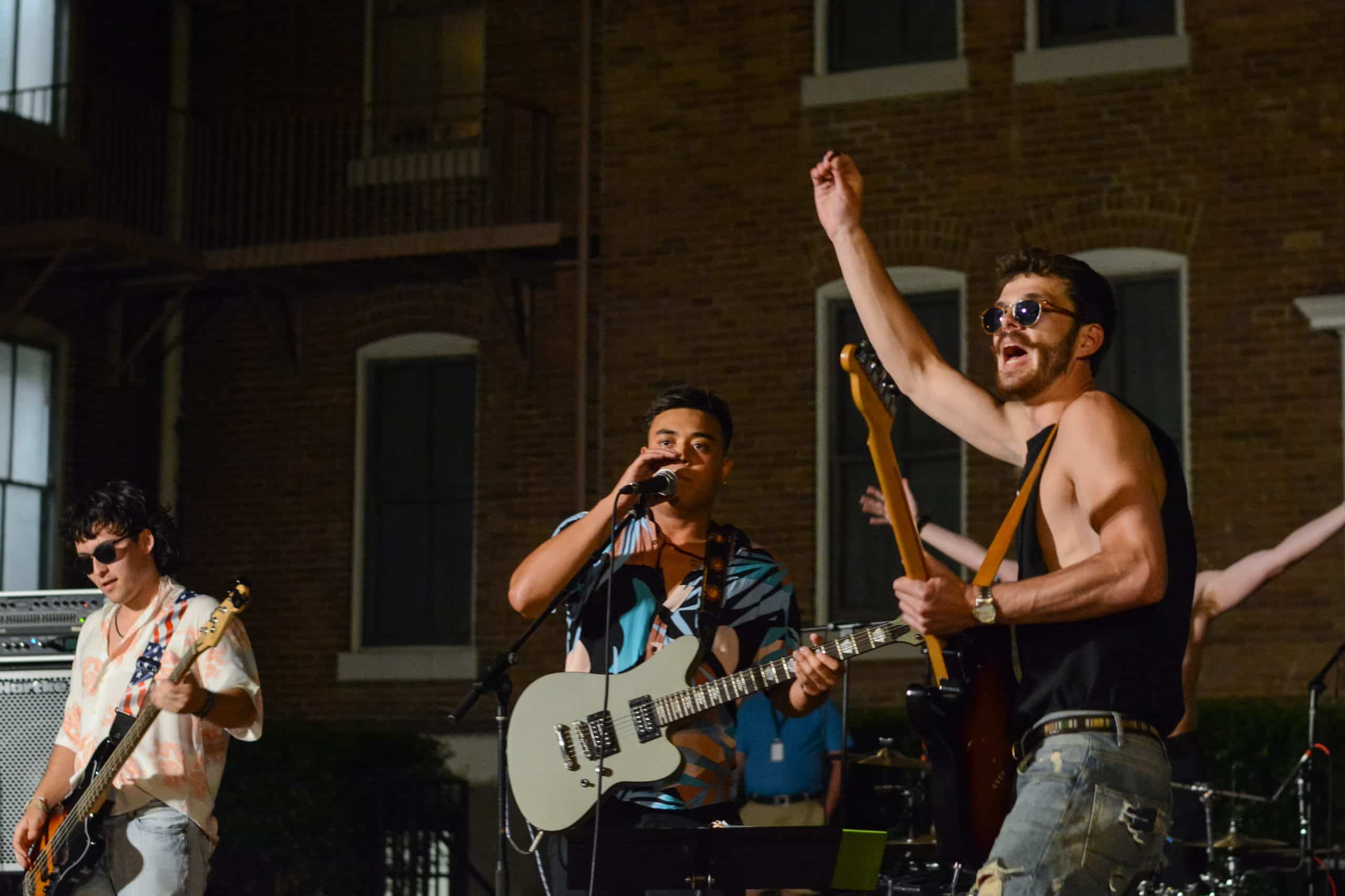 A group of men playing guitar in front of a brick building in Camptown.