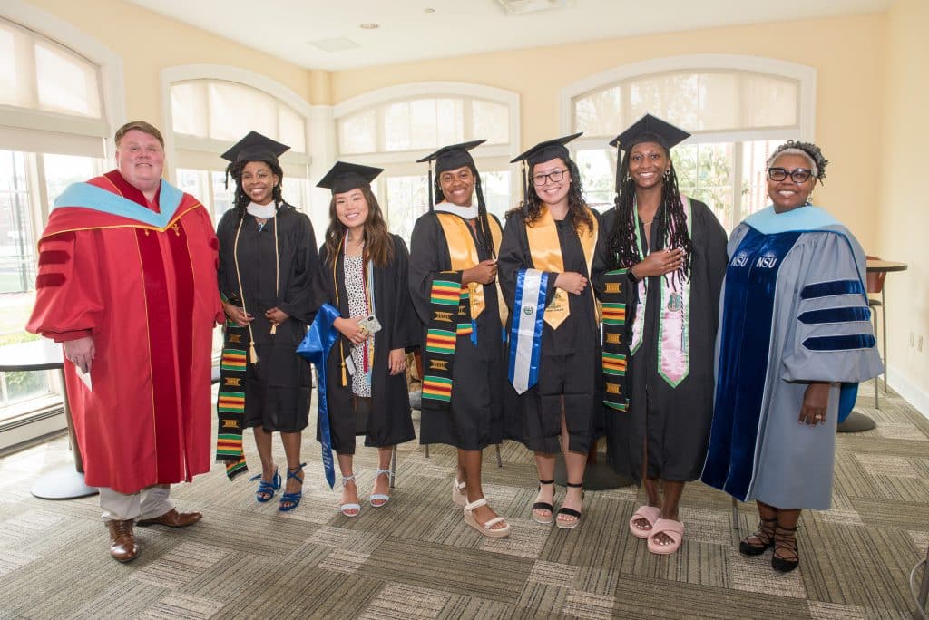 A group of multicultural graduates pose for a photo in regalia 