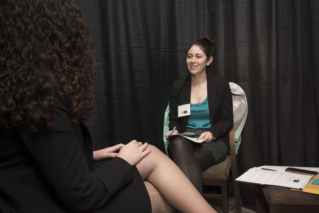 Two women discussing resources for employers while seated in a chair.