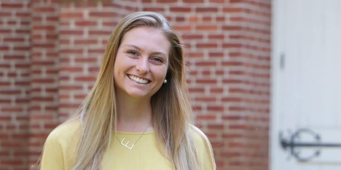 A young woman smiling in front of a brick building.