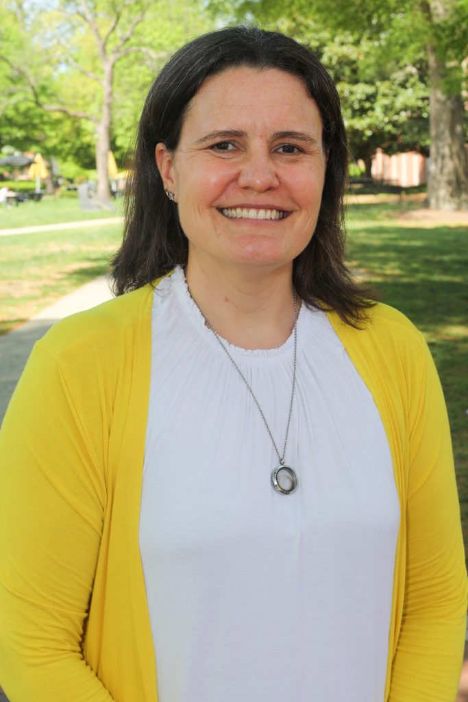 Erin McDonnell-Jones stands outdoors on a sunny day with trees and grass in the background.