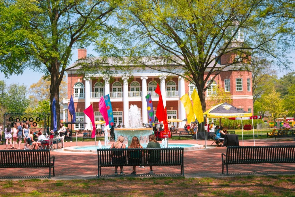 A group of people sitting on benches in front of a Camptown fountain.