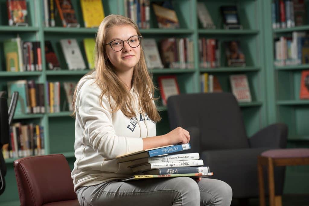 A girl surrounded by a pile of books, engaging in educational experiences and outcomes.