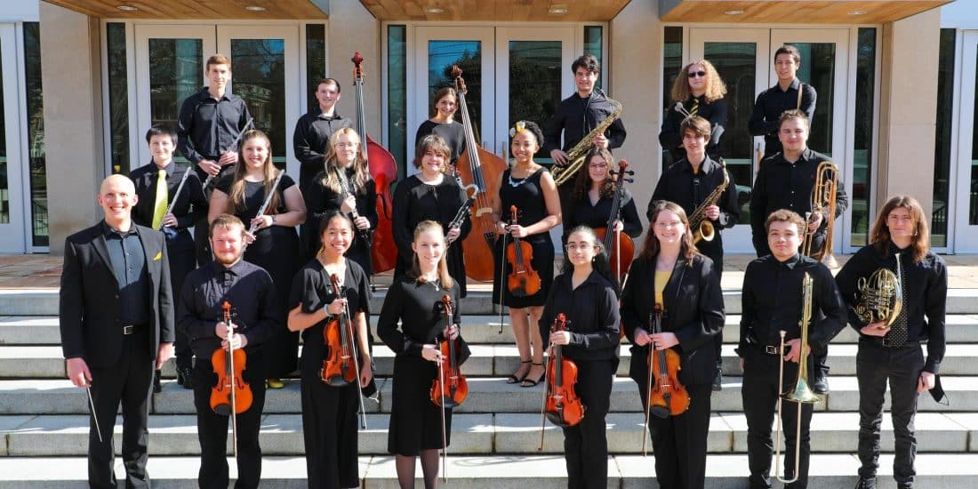The RMC intrumental group standing on steps in front of a building posing for a group photo while holding their musical instruments