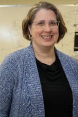 Rebecca Holcombe Michelsen, a woman in glasses, smiling in front of a whiteboard.
