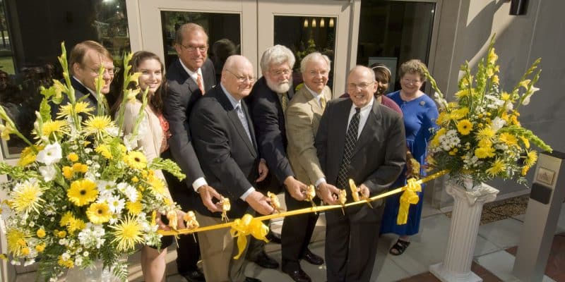 A group of people cutting a ribbon in front of a building.