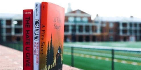 Three books stacked on a brick wall in front of a football field showcasing RMC’s Honors Program and resilience.