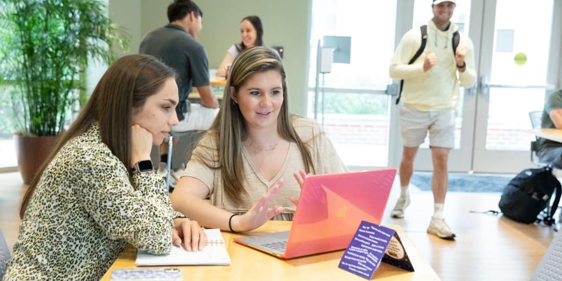 Student getting support from professor sitting at a table.