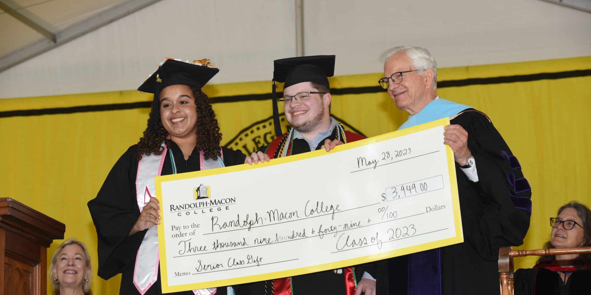 Two students and President Lindgren pose with a giant check during commencement.