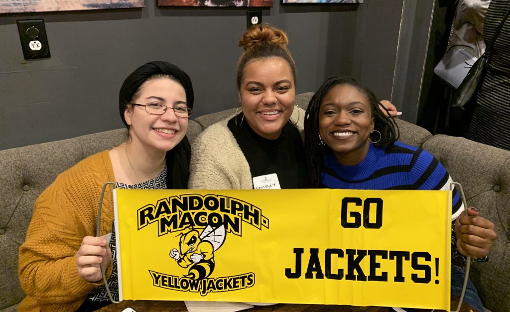 Three RMC Alumni pose with a "Go Jackets!" banner at a happy hour event