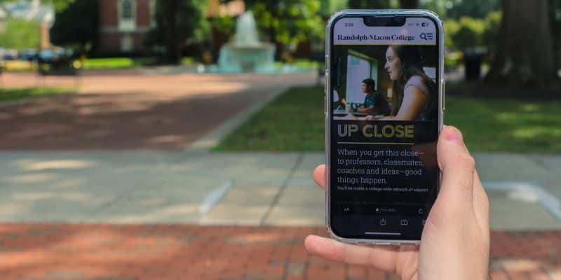 A person holding up a cell phone with the newly redesigned RMC website displayed