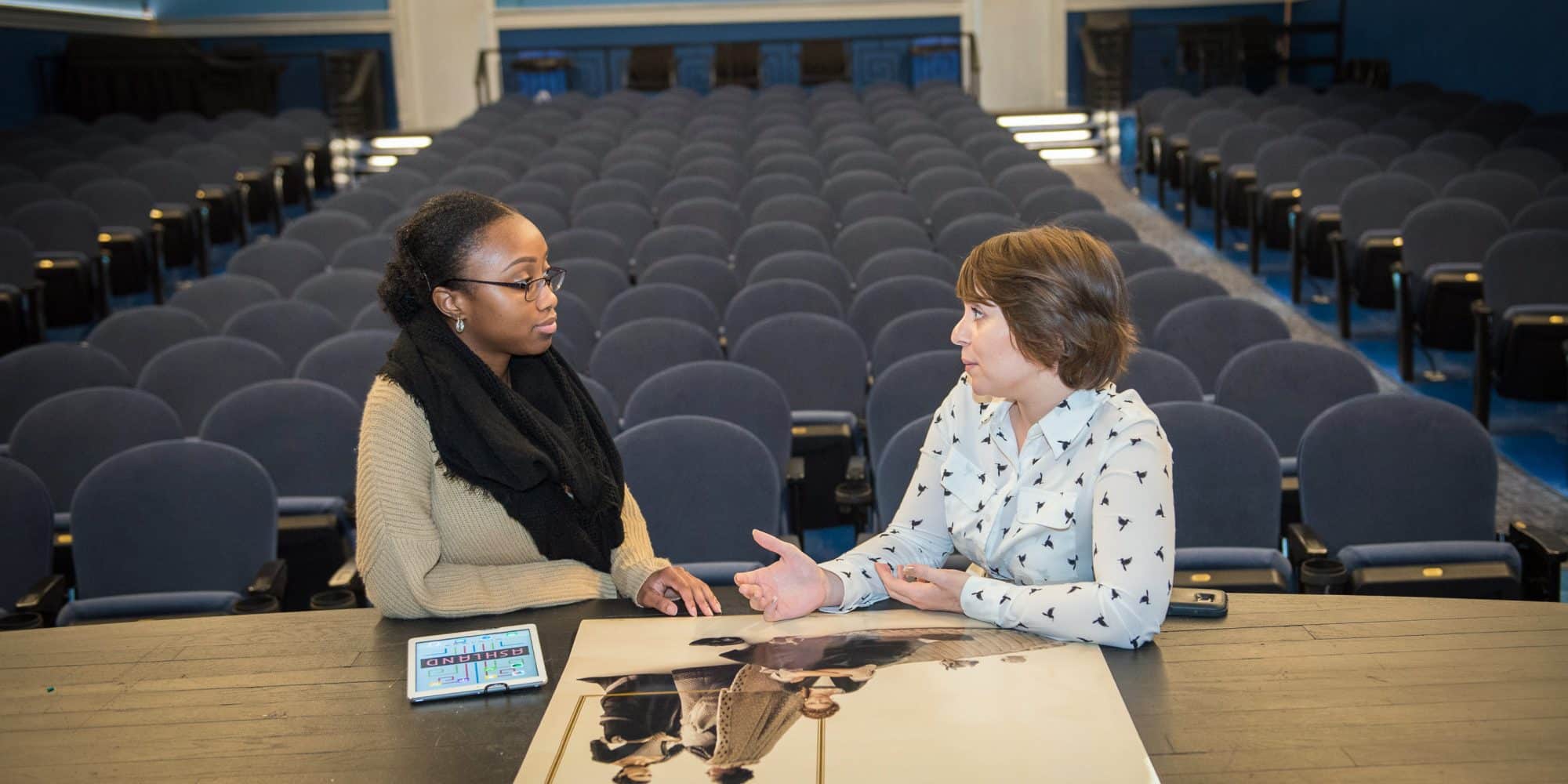 Two women engaging in career preparation at a table in an auditorium.