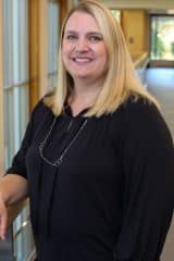 Emily French, a smiling woman in a black shirt standing in a hallway.