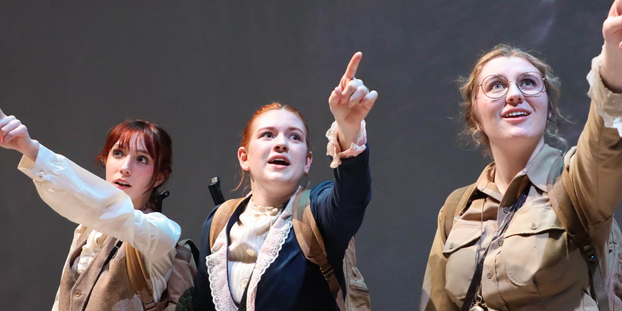 Three women in a play, pointing their fingers in the air