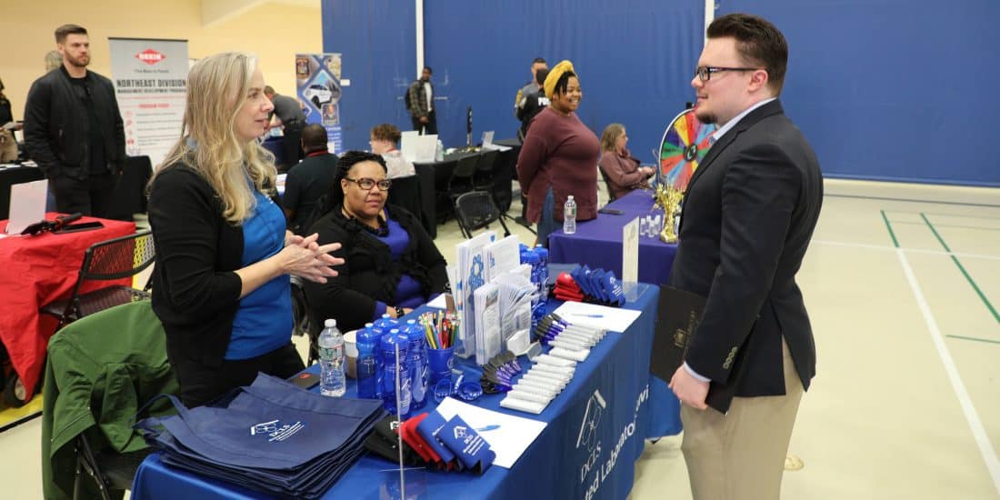 A man and woman talking at a table at a job fair.