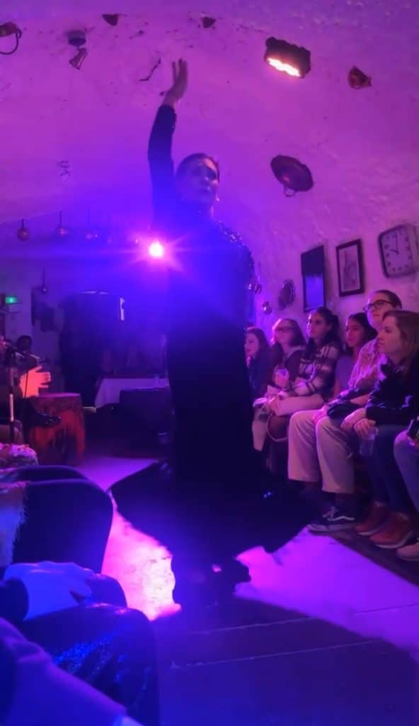 A woman is performing a flamenco dance in a dark room.