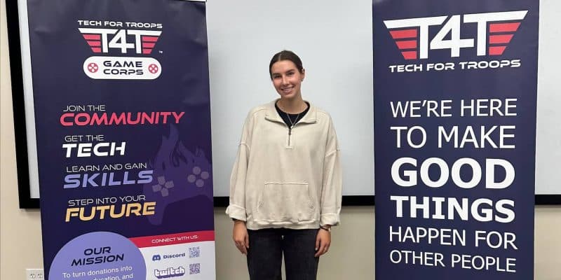 A young woman standing in front of a Tech for Troops banner.