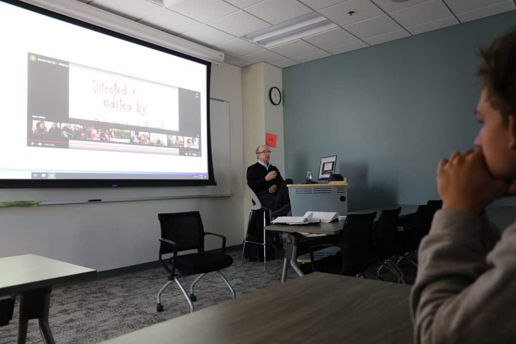 A person in a classroom watching a presentation on a large screen.
