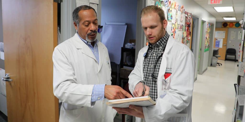 Two doctors in lab coats looking at a book.