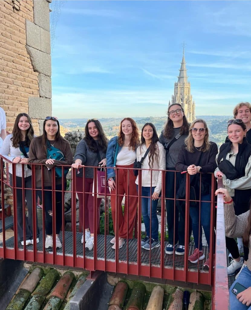 A group of young people posing for a picture on a roof with a church spire in the background.