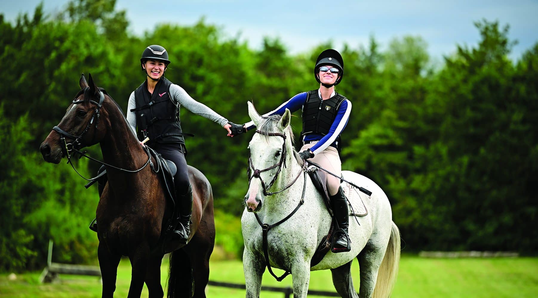 Two Eventing Team Members holding hands while riding outside.