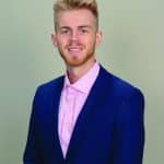Professional young man in a blue suit with a pink shirt smiling for a portrait.
