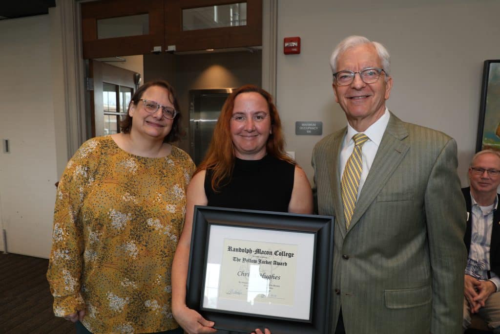 Three individuals posing with an award certificate, two women flanking a man in a suit.