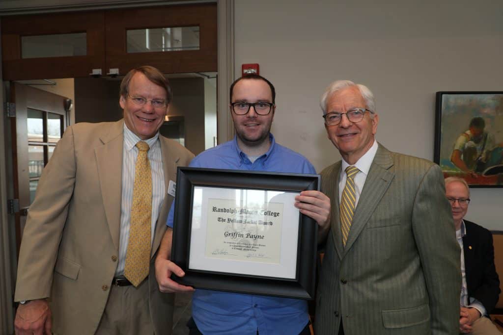 Three men posing for a photo, with the middle one holding a framed certificate.