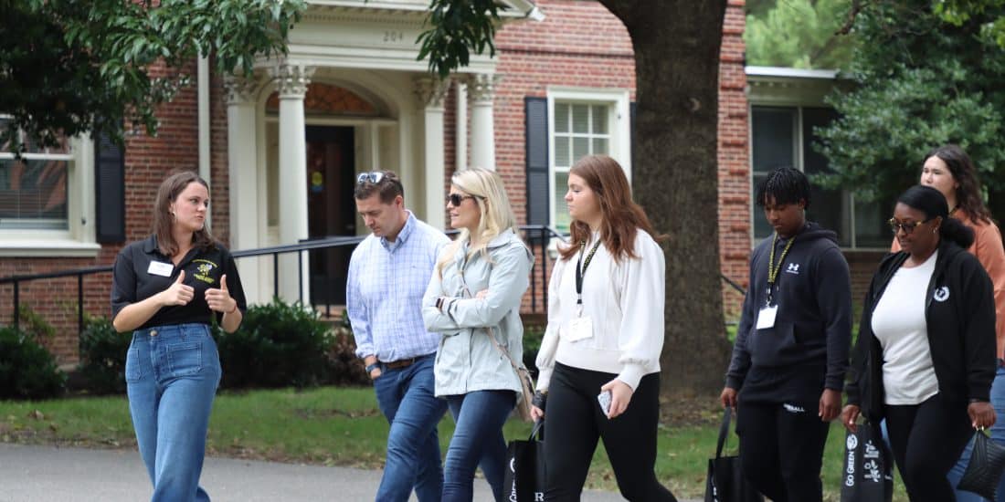 A college guide leading a tour for prospective students and parents outside a campus building during one of the scheduled college visits.