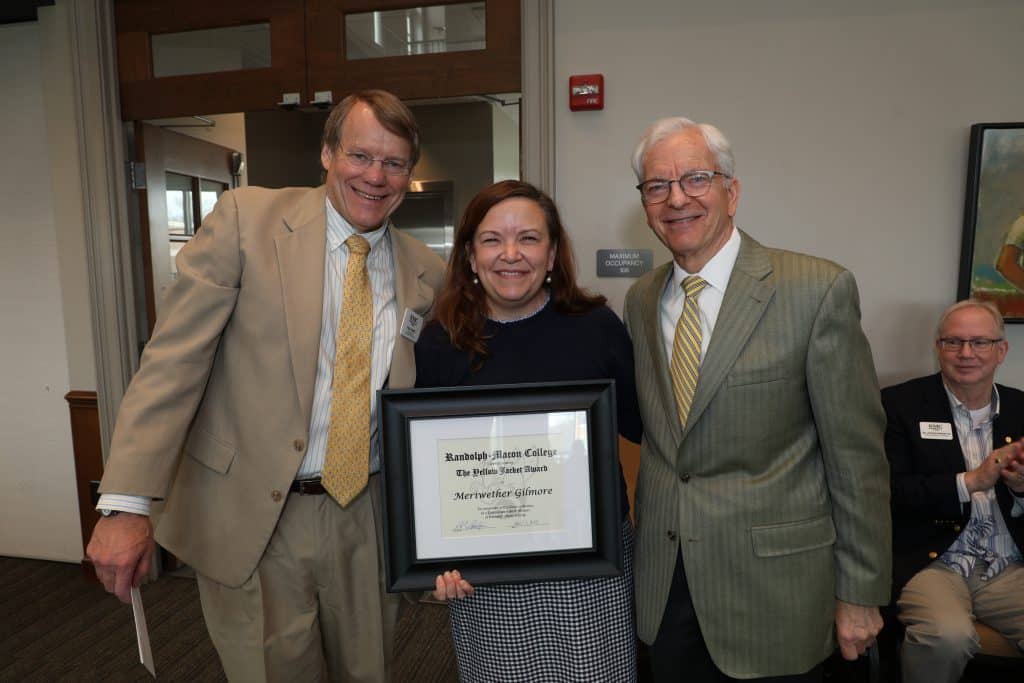 Three individuals posing for a photo at an award ceremony, with the central person holding a framed certificate.