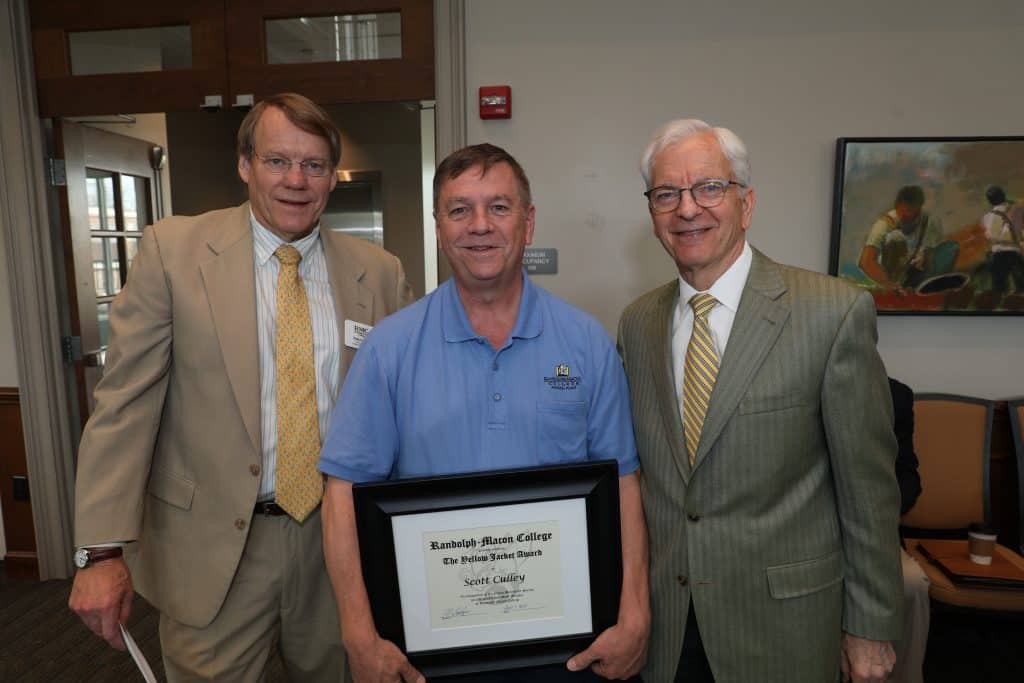 Three men smiling, with the middle one holding a framed certificate.