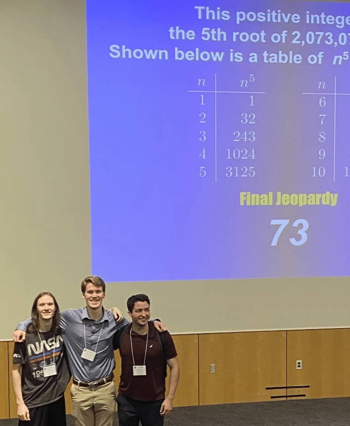 Three people stand in front of a Final Jeopardy screen displaying a math question and the number 73, posing for a photo in a classroom or lecture hall.