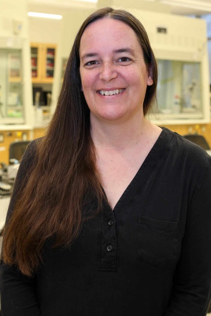 Nora Green smiles while standing in a laboratory setting.
